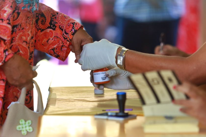 An election clerk dipping the finger of a voter in indelible ink.